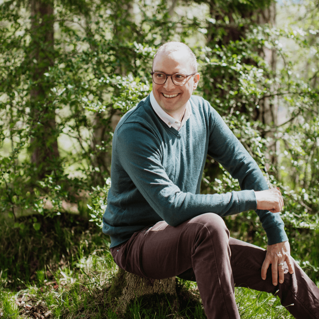 Lukas Leitner sitzt im Wald und lächelt