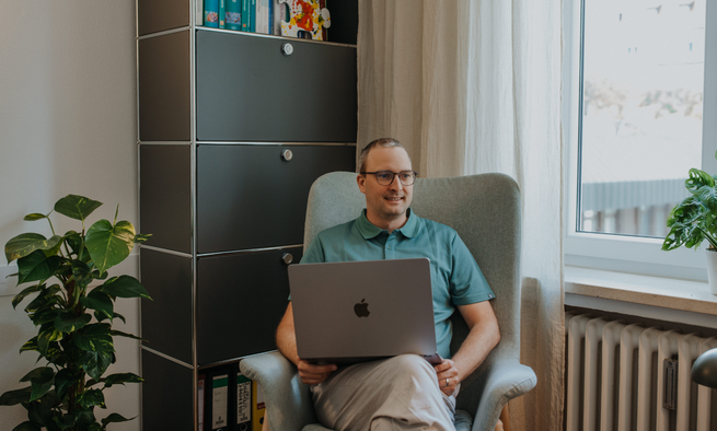 Lukas Leitner sitzt in seinem Behandlungszimmer und hat einen Laptop auf dem Schoß.